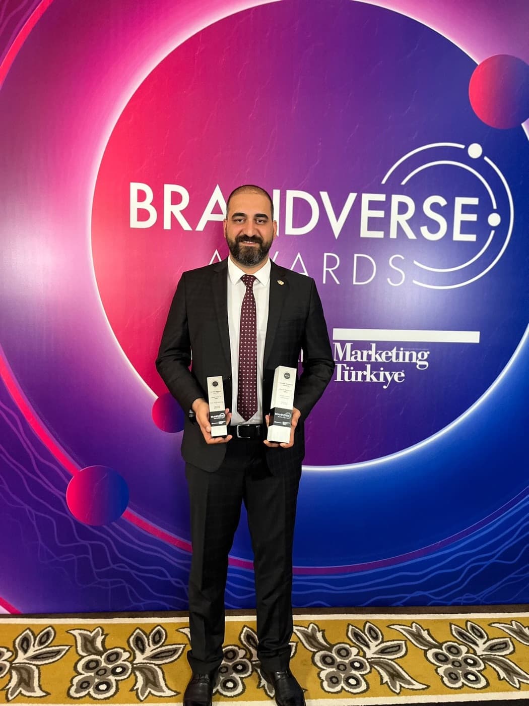 Ozgur Safak Okmek holding two Brandverse Awards trophies